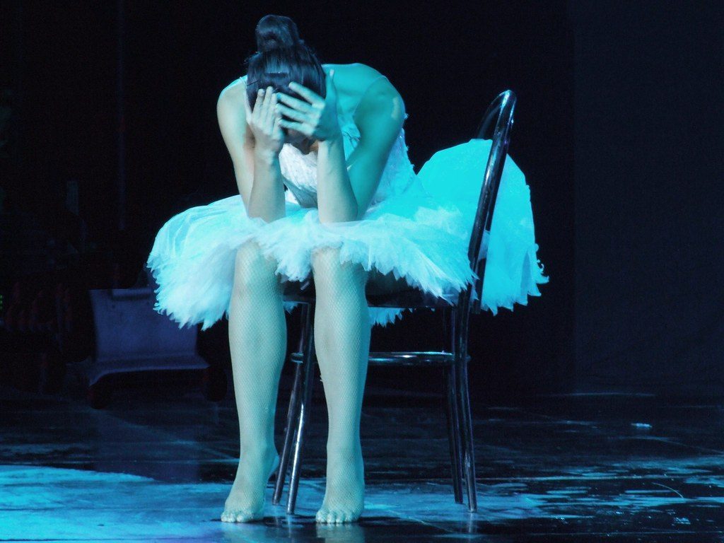 A dancer seated alone on a lit stage